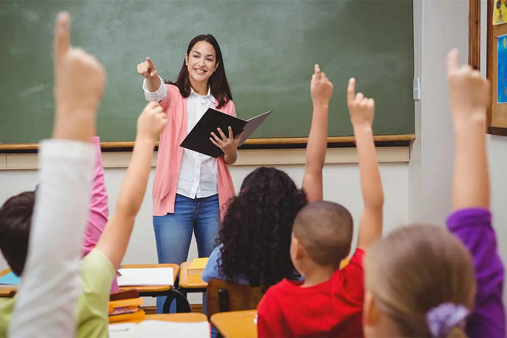 teacher in classroom children hands up
